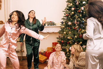 New Year pajama home party. Young women in pajamas dancing near the Christmas tree in the living...