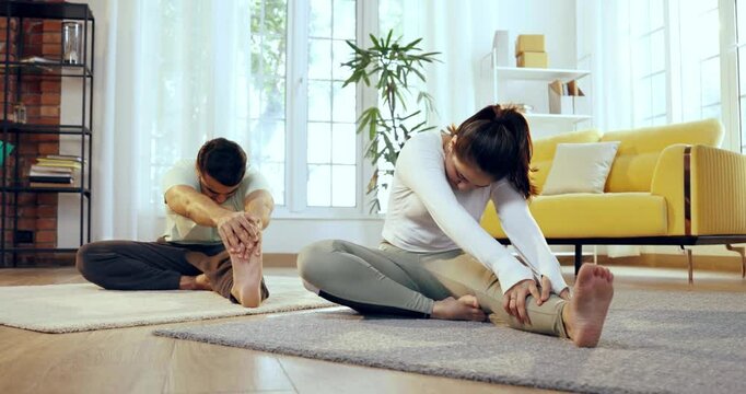 Indian Asian young couple learning yoga in the comfort of their lavish home, performing janu shirasana or head to knee pose together, enhancing flexibility and mindfulness in a serene environment
