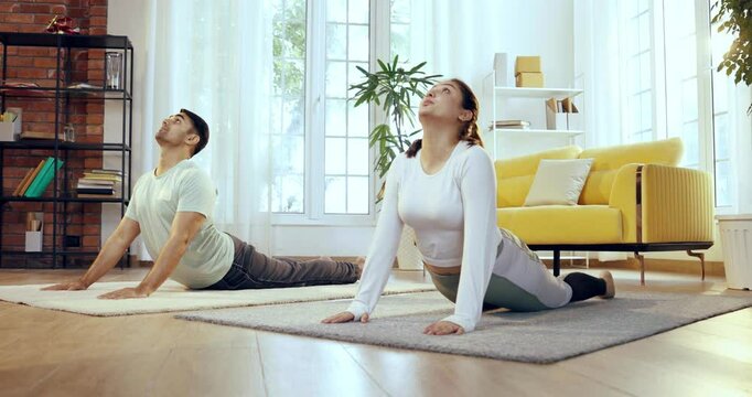 Indian Asian young couple learning yoga in the comfort of their lavish home, practicing bhujangasana or back bend pose together to enhance flexibility and improve spinal strength