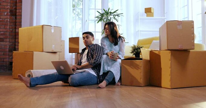 Indian Asian couple happily settling into their new home, surrounded by carton or boxes. The husband designing the room layout, while the wife makes suggestions, enjoying the moment of collaboration