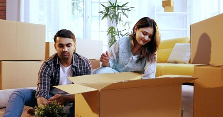 Indian Asian young couple enjoying a heartwarming moment as they unpack their belongings in a new home, smiling while holding a cherished photo frame that brings back memories of their past