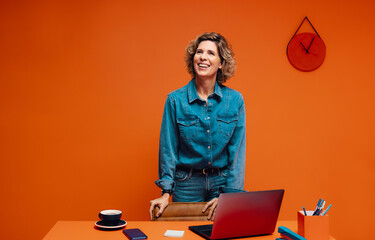 Confident female manager using laptop in a bold orange contemporary office space