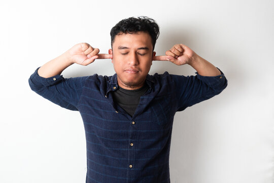 Adult Asian man with eyes closed while covering his ears with finger