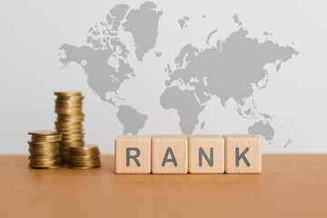 RANK text on wooden cube blocks and blurred stack of coins with world map background