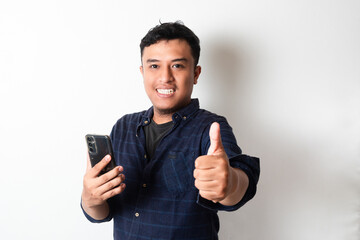 Adult Asian man wearing dark blue flannel shirt smiling and give thumb up while holding mobile phone