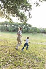 Mother and son running together through park on sunny day