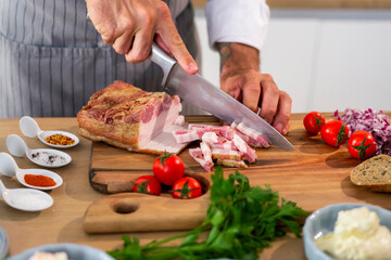 Chef cutting bacon on wooden board with sharp knife