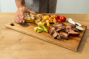 Chef placing glass of whiskey near sliced steak on wooden board