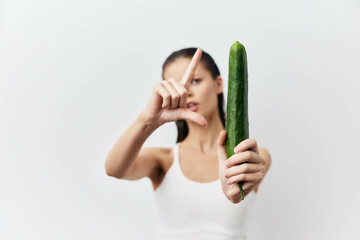 Woman holding a cucumber in front of a white background, showcasing a playful pose while framing the vegetable with her hands, emphasizing freshness and health