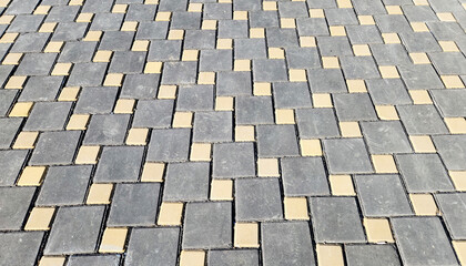 Fototapeta premium Sidewalk tiled with the concrete square gray and yellow paver blocks in along a street 