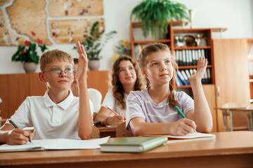 With hands up. Pupils, kids in the classroom together