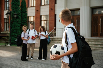Boy is with soccer ball. Kids are near the school together, pupils