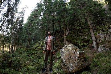 Obraz premium Man hiking through a dense forest in the Carpathian Mountains, surrounded by lush greenery and rocky terrain. Perfect for adventure travel, nature exploration, and outdoor lifestyle content.
