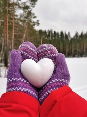 Fototapeta premium Person holding a heart-shaped snowball with colorful gloves in a snowy forest setting. Winter activities concept.