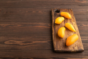 Yellow tomatoes on cutting board on brown wooden. Side view, copy space