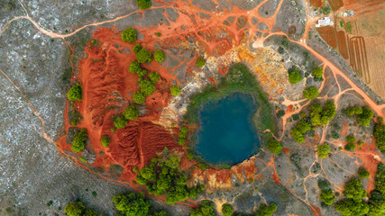 Perpendicular aerial view of the Otranto bauxite quarry in the province of Lecce, Salento, Puglia, Italy. A natural lake has been created inside the disused mine. The water has a deep blue colour.