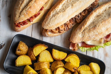Three baguettes filled with different ingredients and a tray of potato wedges