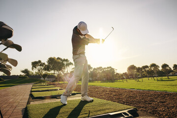 Professional golfer practicing his swing in the sunlight at a beautiful golf course