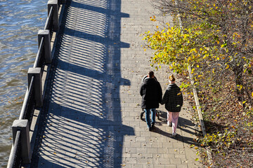 Couple with baby pram walking on river embankment at autumn city park, aerial view