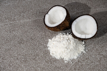 Coconut flour among coconut halves on gray stone background, place for text