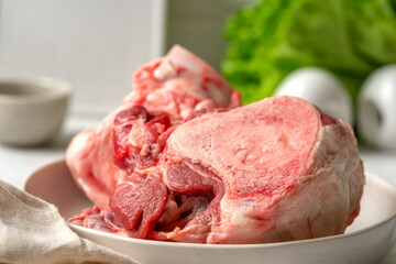 Raw beef bones for making broth in a white plate on a culinary kitchen table closeup