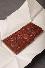 whole but broken bar of dark chocolate with grinded cocoa beans on kraft paper package, close up shot