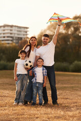 Family of father, mother, daughter and son that are standing in the field, with kite in hand