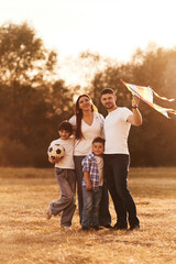 Fototapeta premium Vacation time. Family of father, mother, daughter and son that are standing in the field, with kite in hand