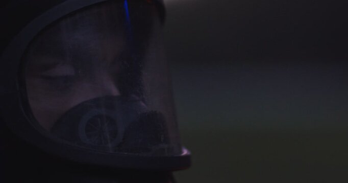 Close up of Caucasian male face in mask and helmet. Man in respirator and casque with serious look. Darkness outdoor. Concentrated firefighter.