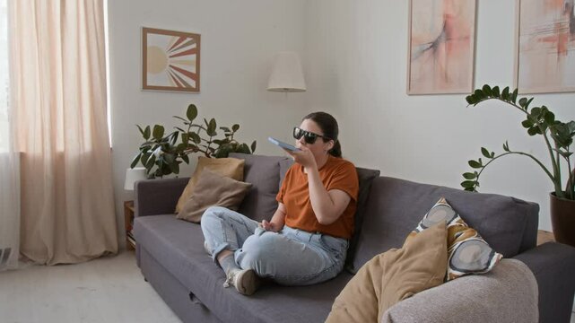 Girl with visual impairment chatting with friends via voice messages while sitting on couch in living room