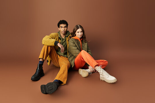 A stylish couple dressed in vivid autumn attire poses together in warm tones, exuding charm.
