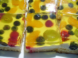 Fruit cake, sponge cake with yellow jelly and colorful fruits - tasty refreshing dessert background, close-up shot. Topics: season, natural vitamins, health, sweet, diet, food, vegetarian