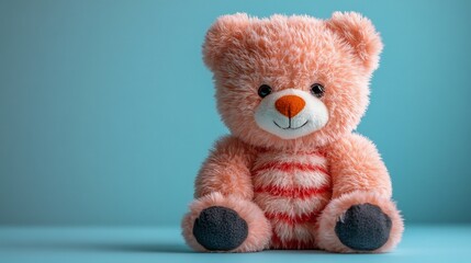 Obraz premium Plush bear toy with redandwhite stripes black paws and an orange snout sits on a lightblue surface against a skyblue background adding a cozy and friendly vibe
