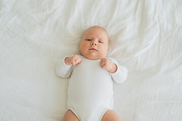 Happy baby. Cute little newborn girl with smiling face lying on bed in bedroom. Infant baby resting playing lying down on white blanket at home. Motherhood happy child childcare concept