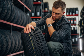 Thinking, sitting. Man worker is maintenance station with tires, wheels