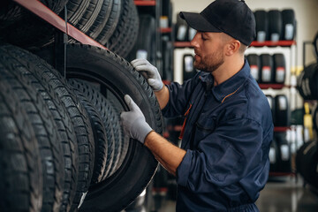 On the shelve, taking the tire. Man worker is maintenance station with tires, wheels