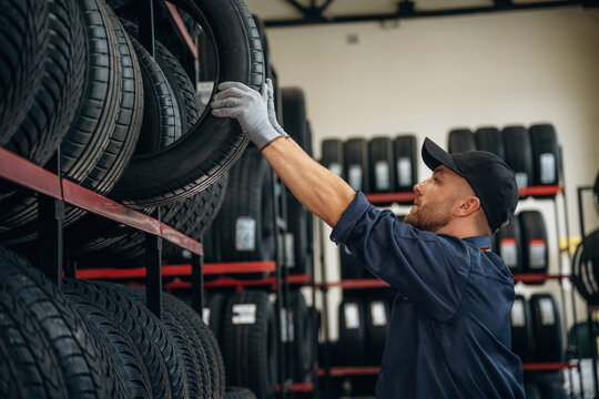 On the shelve, taking the tire. Man worker is maintenance station with tires, wheels