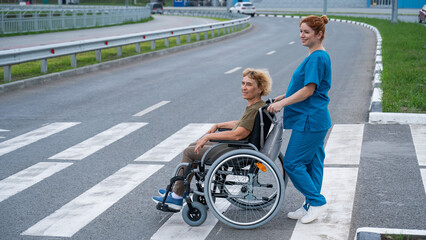 Red-haired nurse pushing an elderly woman in a wheelchair across the road. 