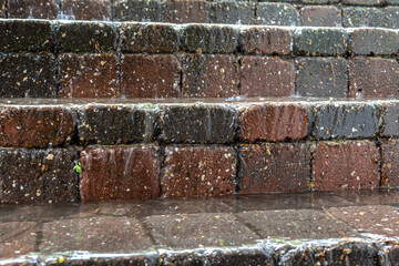 Close-up of wet brick steps during a downpour, with water accumulating on the surface, showing slick conditions and risks associated with bad weather, moisture and outdoor surfaces during heavy rain.