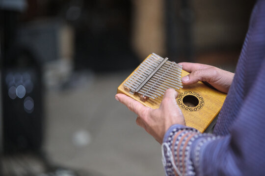 Kalimba instrument played by a man wearing a poncho with a workshop in the background