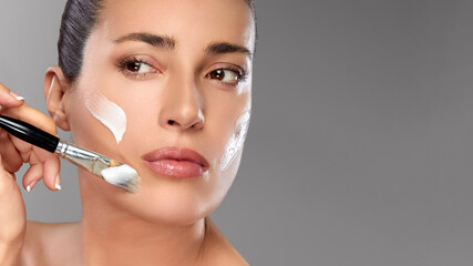 Woman applying face mask with a brush for skincare and beauty routine on a neutral background