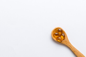 Vitamin omega capsules in a spoon on a colored background. Pills served as a healthy meal. Red soft...