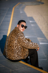 Krean guy in a leopard fur coat sits on the steps in the autumn park of Busan Beach