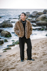 A Korean guy in a leopard fur coat walks along the beach against the backdrop of the autumn landscape of Busan Haeundae.