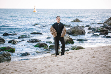 A Korean guy in a leopard fur coat walks along the beach against the backdrop of the autumn landscape of Busan Haeundae.