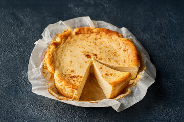 Close-up of a Basque burnt cheesecake with a caramelized top and a slice removed, revealing its creamy interior. Set against a dark background, it highlights the dessert s rustic and artisanal appeal.