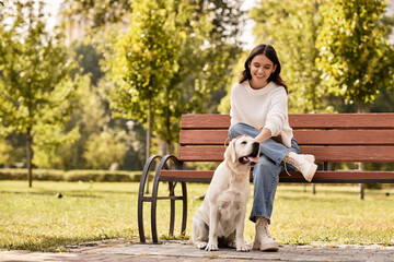 Delighted woman in cozy autumn wear interacts with her playful dog on a sunny park bench.