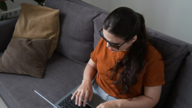 High angle view of visually impaired young woman with sunglasses surfing internet on laptop in living room