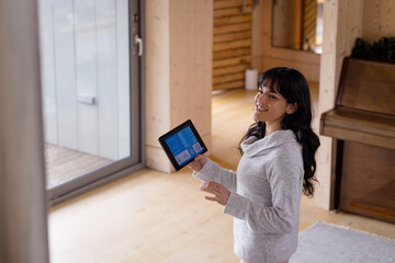 Smiling woman using tablet to control smart home system in cozy living room