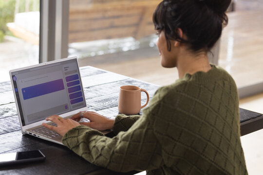 Woman chatting online using laptop at home, enjoying coffee break